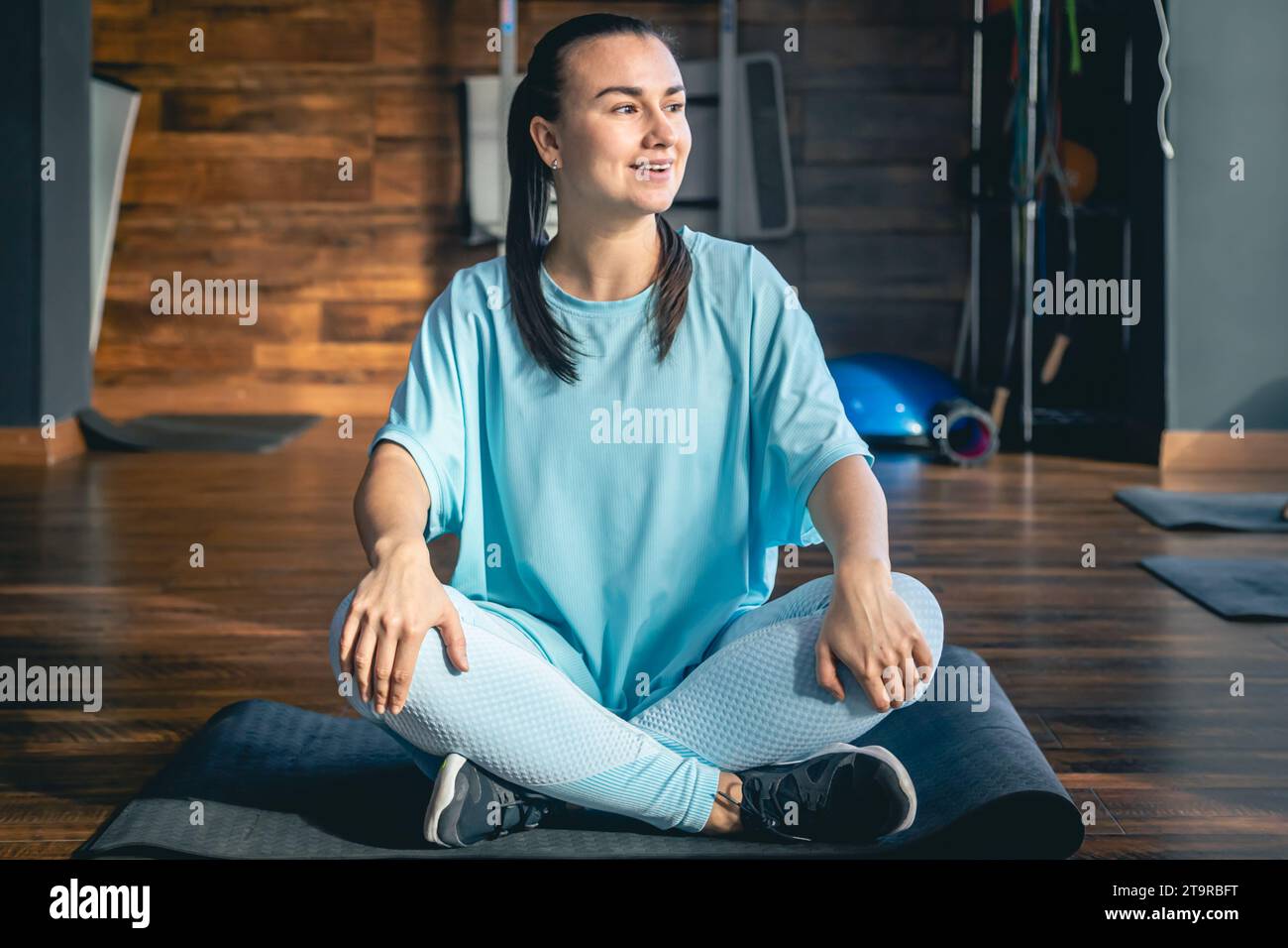 Young woman sitting on a mat in a fitness center, doing yoga and ...