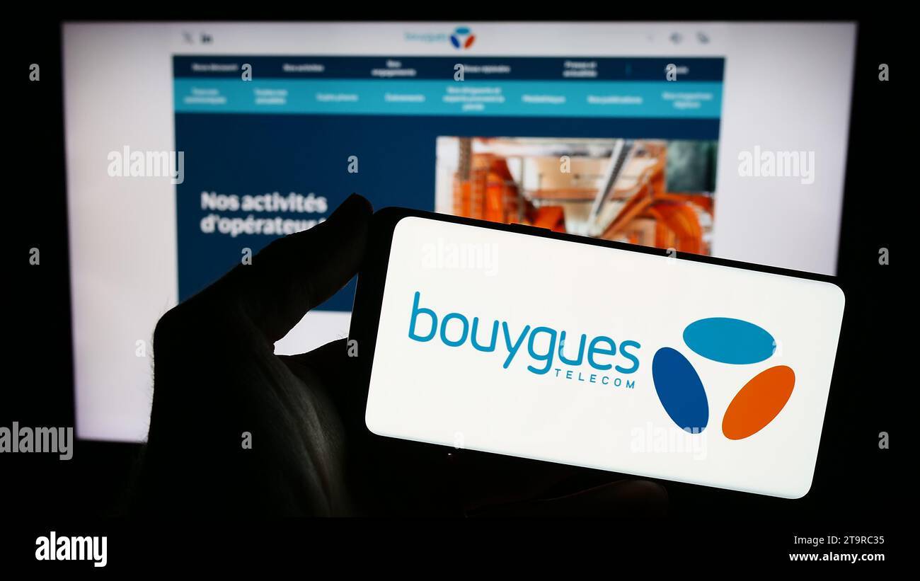 Person holding smartphone with logo of French telecommunications company Bouygues Telecom S.A. in front of website. Focus on phone display. Stock Photo