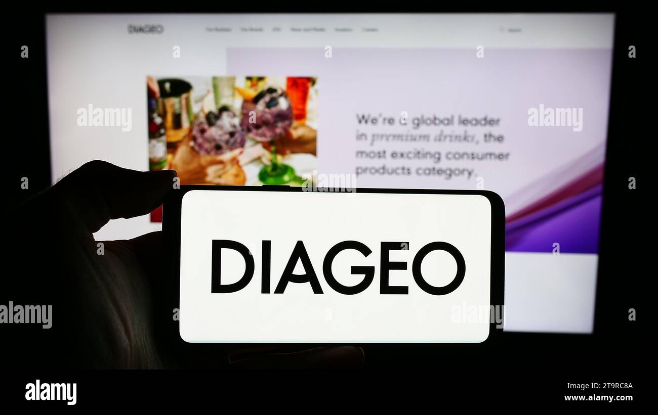 Person holding smartphone with logo of British alcoholic beverage company Diageo plc in front of website. Focus on phone display. Stock Photo