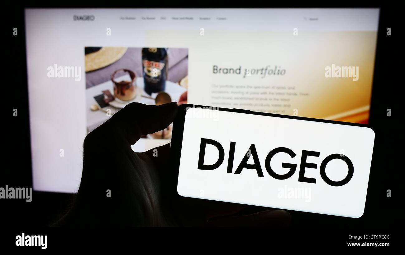 Person holding cellphone with logo of British alcoholic beverage company Diageo plc in front of business webpage. Focus on phone display. Stock Photo