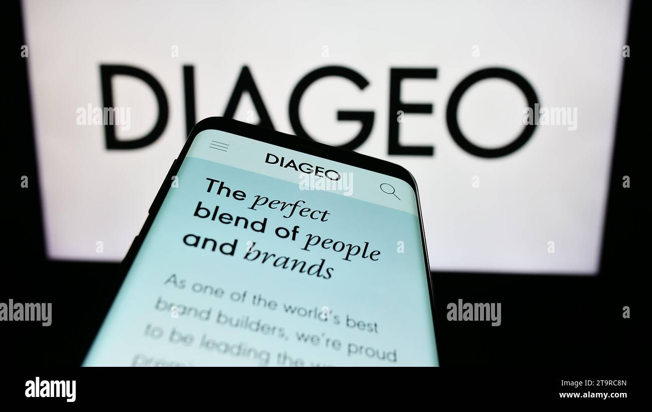 Mobile phone with webpage of British alcoholic beverage company Diageo plc in front of business logo. Focus on top-left of phone display. Stock Photo