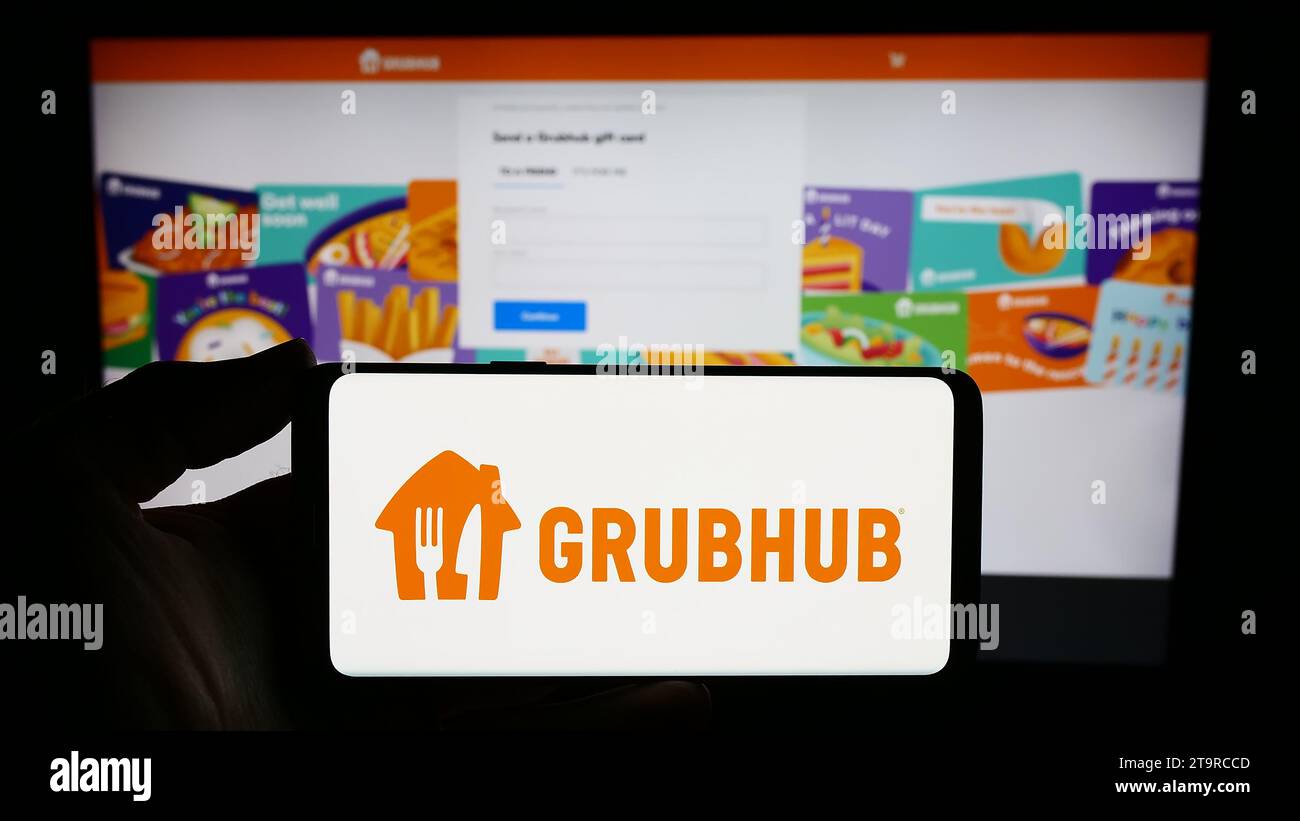 Person holding smartphone with logo of US food ordering and delivery company Grubhub Inc. in front of website. Focus on phone display. Stock Photo