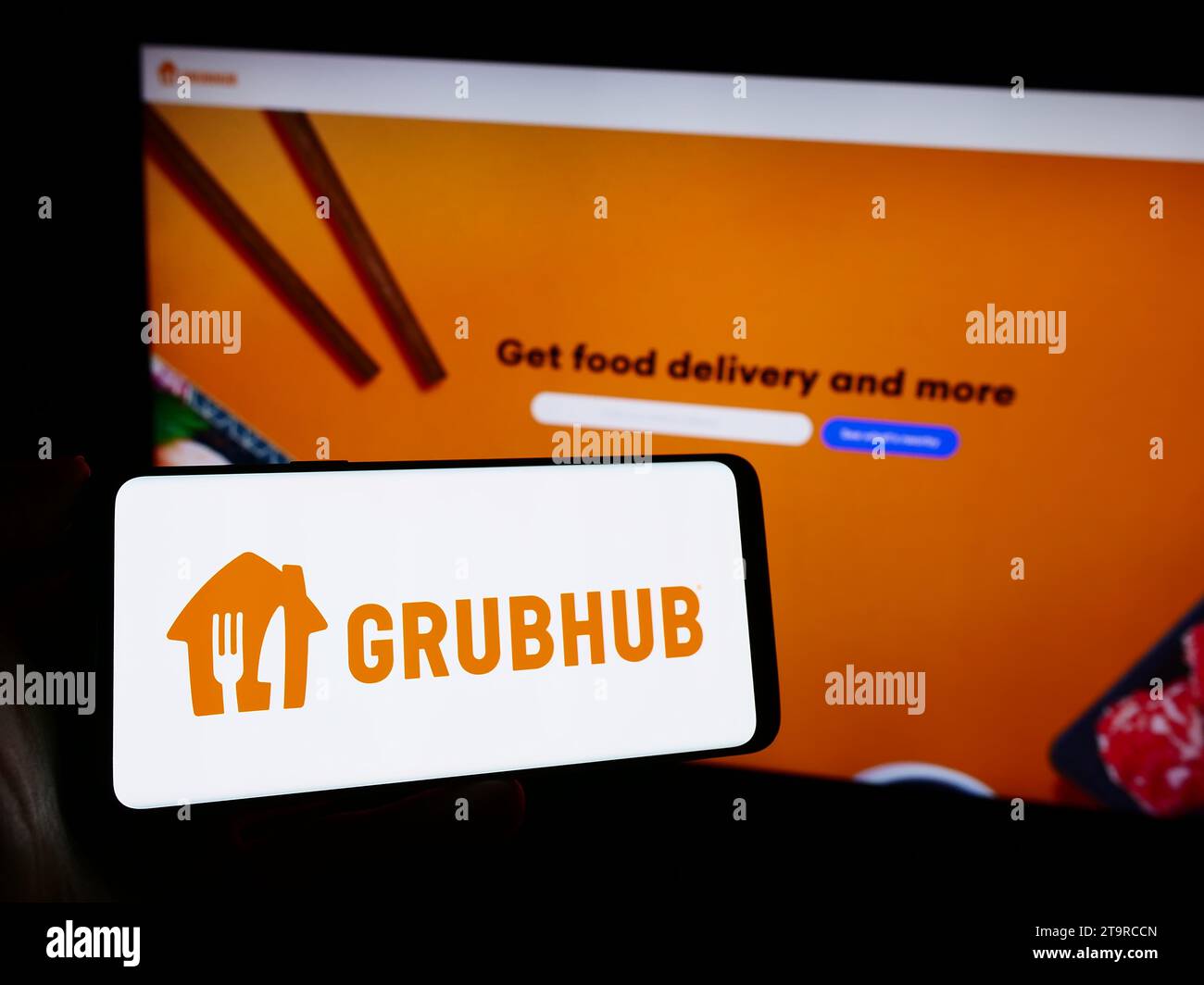 Person holding cellphone with logo of US food ordering and delivery company Grubhub Inc. in front of business webpage. Focus on phone display. Stock Photo