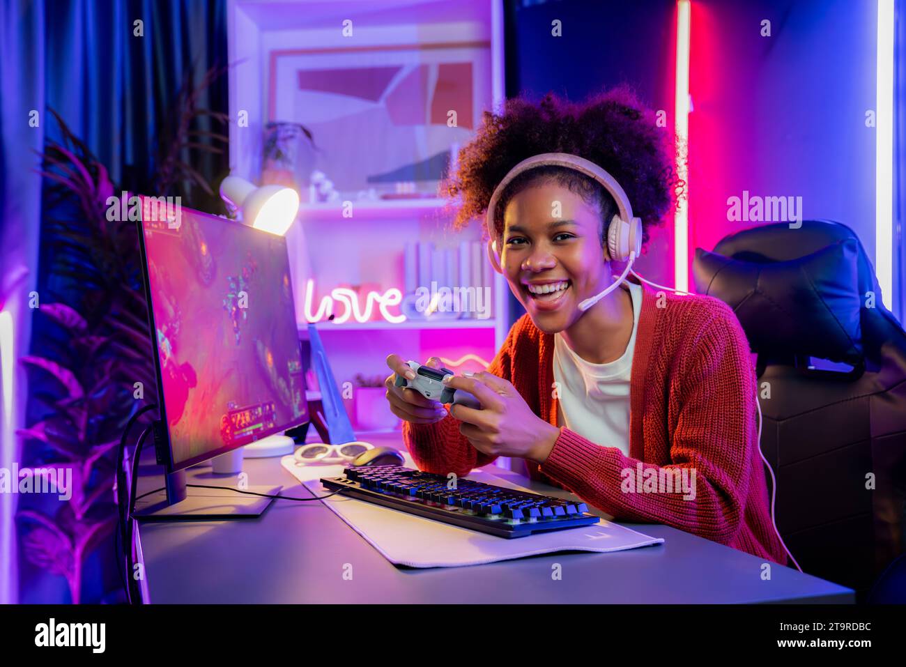 African American girl gaming streamer team winner playing online fighting with Esport wearing headphones in neon lighting room. Talking other players Stock Photo