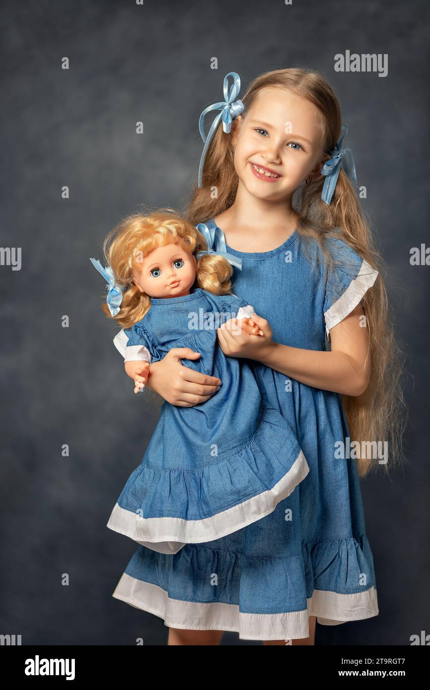 Portrait of ?ute girl child kid and doll isolated on grey background. Child and favorite toy. A gift for a birthday or other holiday. Stock Photo