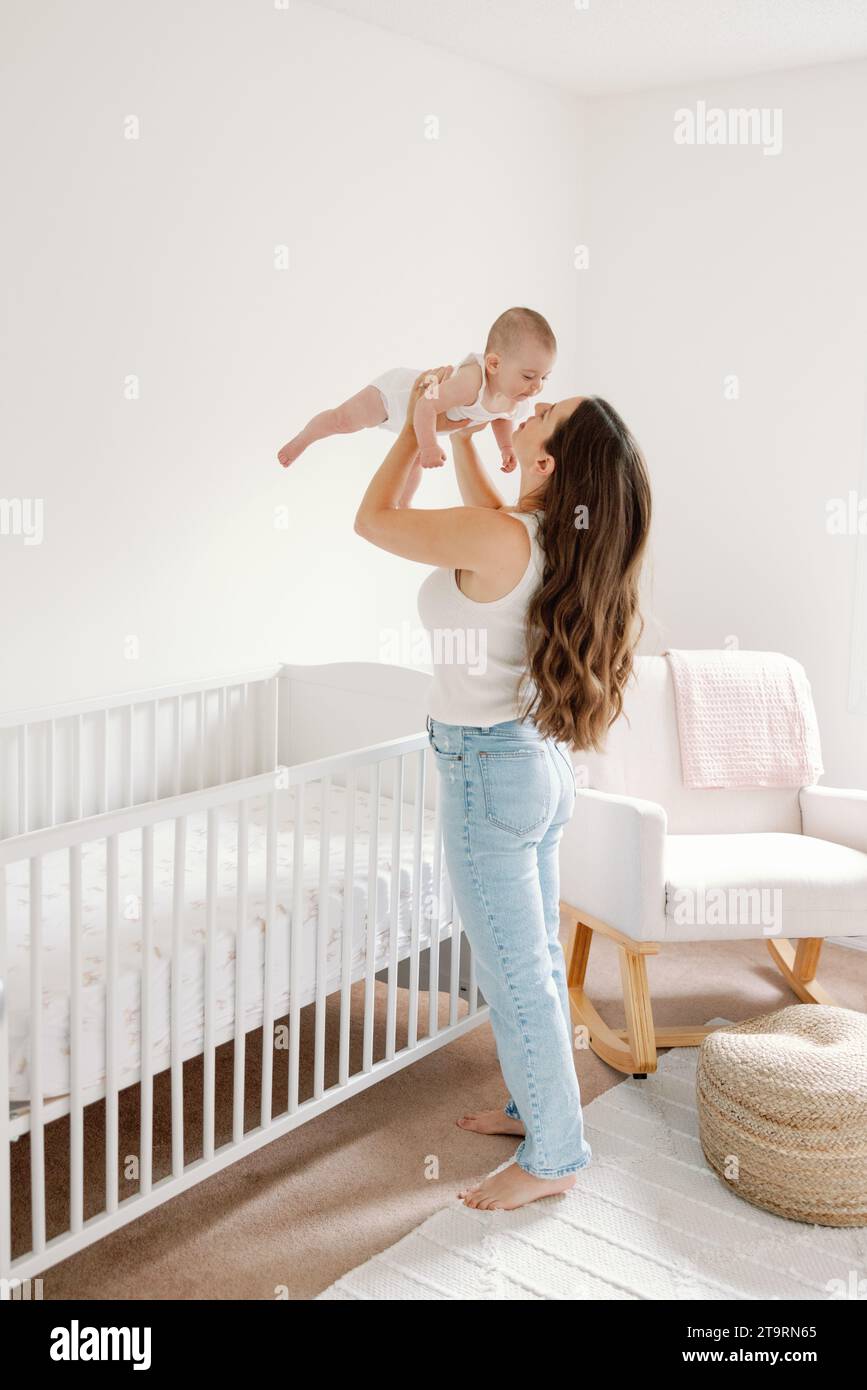 Mom standing in front of crib in neutral nursery holding baby up Stock Photo