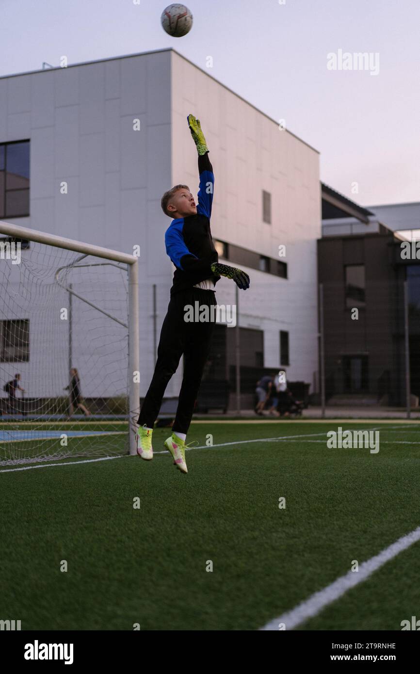Kids playing football, boy goalkeeper catches ball in goal. Stock Photo