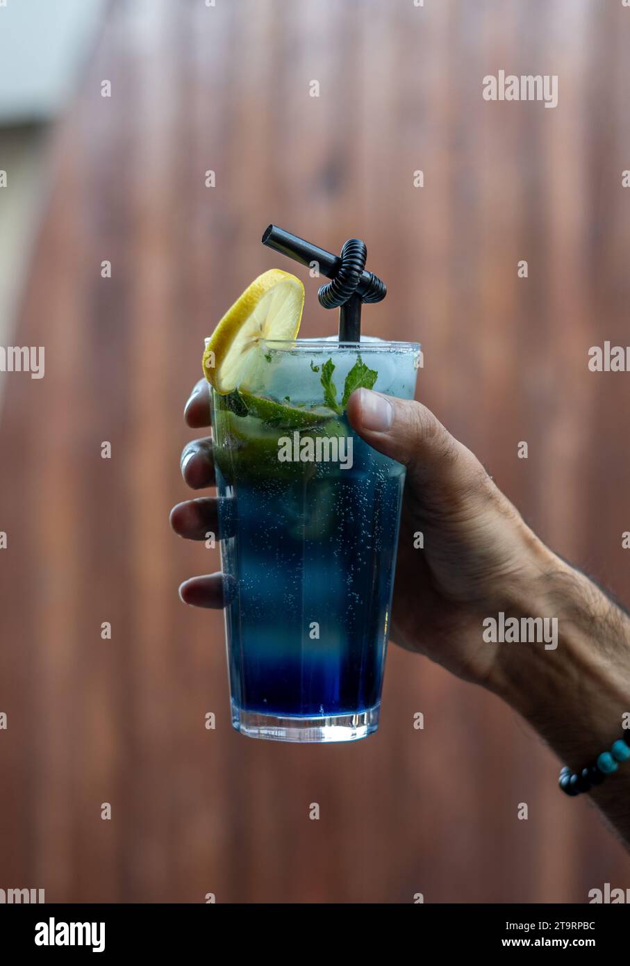 Man Holding a Glass of Cold Drink, a Piece of Lemon is Placed on top of the Glass, Black Drinking Straw Stock Photo