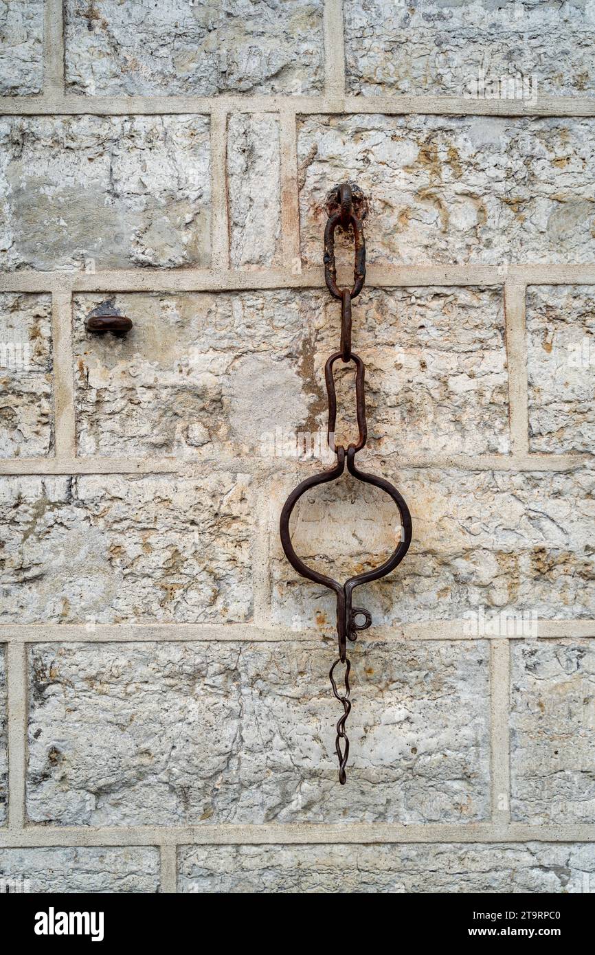 An aged pair of rusty metal handcuffs hanging on a rough, chipped-paint wall Stock Photo
