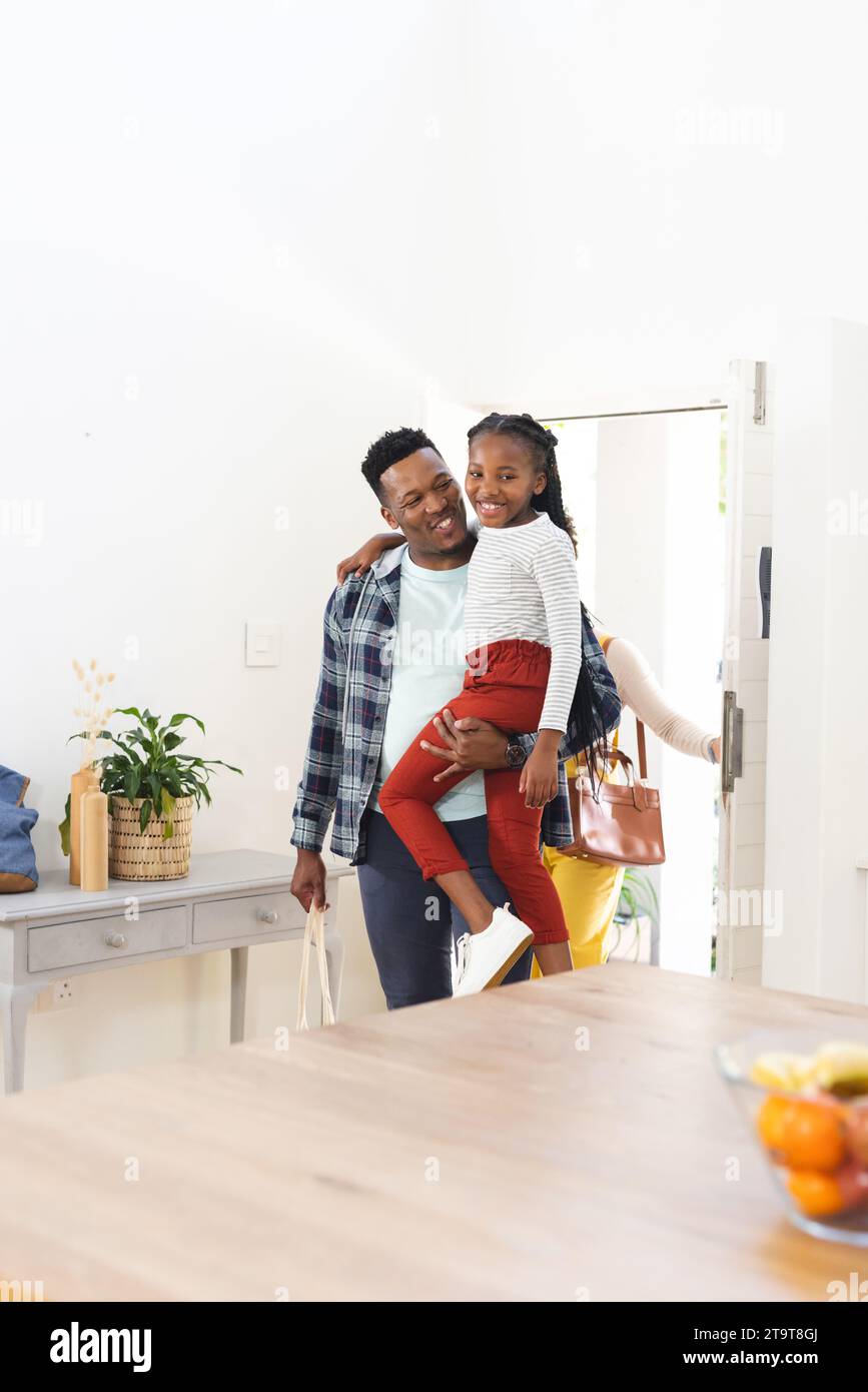 Happy african american family coming home and father holding daughter, copy space. Expression, togetherness, parenthood, childhood and domestic life, Stock Photo