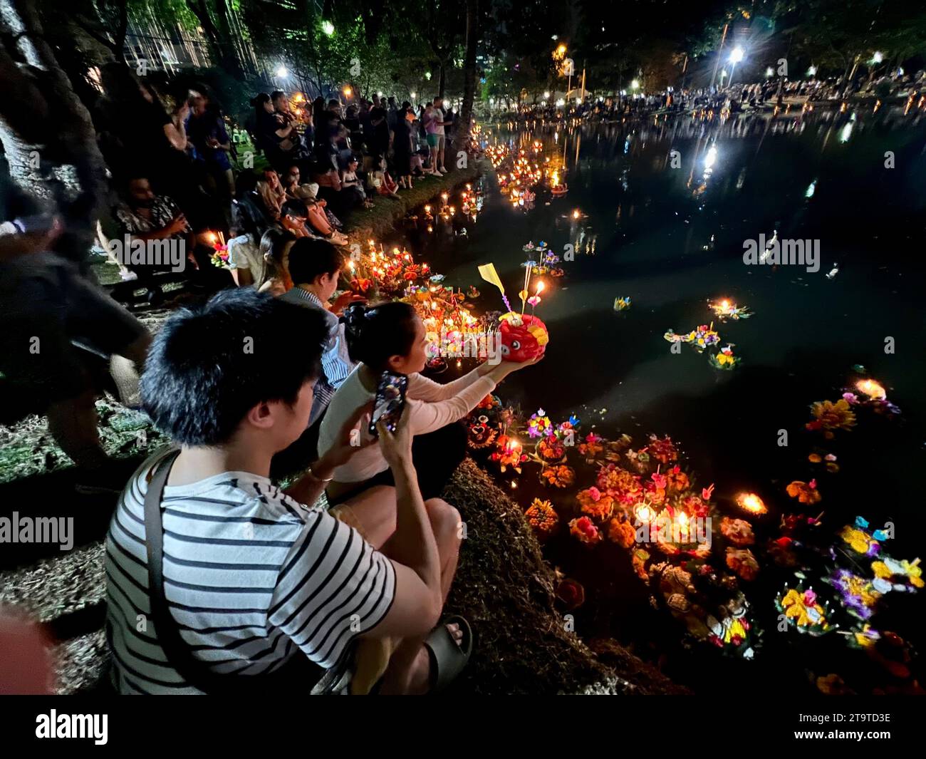 Bangkok, Thailand. 27th Nov, 2023. Thais pray at a lake in Lumphini Park, one of Bangkok's largest parks, before putting their krathong into the water. The small rafts are made of banana trees or expanded polystyrene and are decorated with flowers, incense sticks and candles. Thailand always celebrates the Loi Krathong festival of lights on the day of the full moon in the twelfth month of the traditional calendar. The small rafts are lowered into the water in rivers or lakes to pay homage to the Hindu water goddess Mae Phra Khongkha. Credit: Carola Frentzen/dpa/Alamy Live News Stock Photo