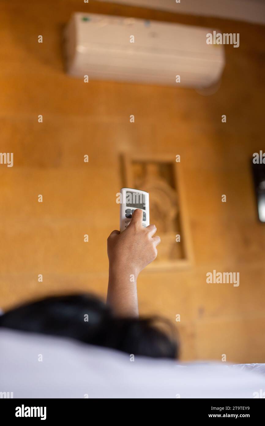 A human hand holding AC remote control pointing towards air conditioner ...
