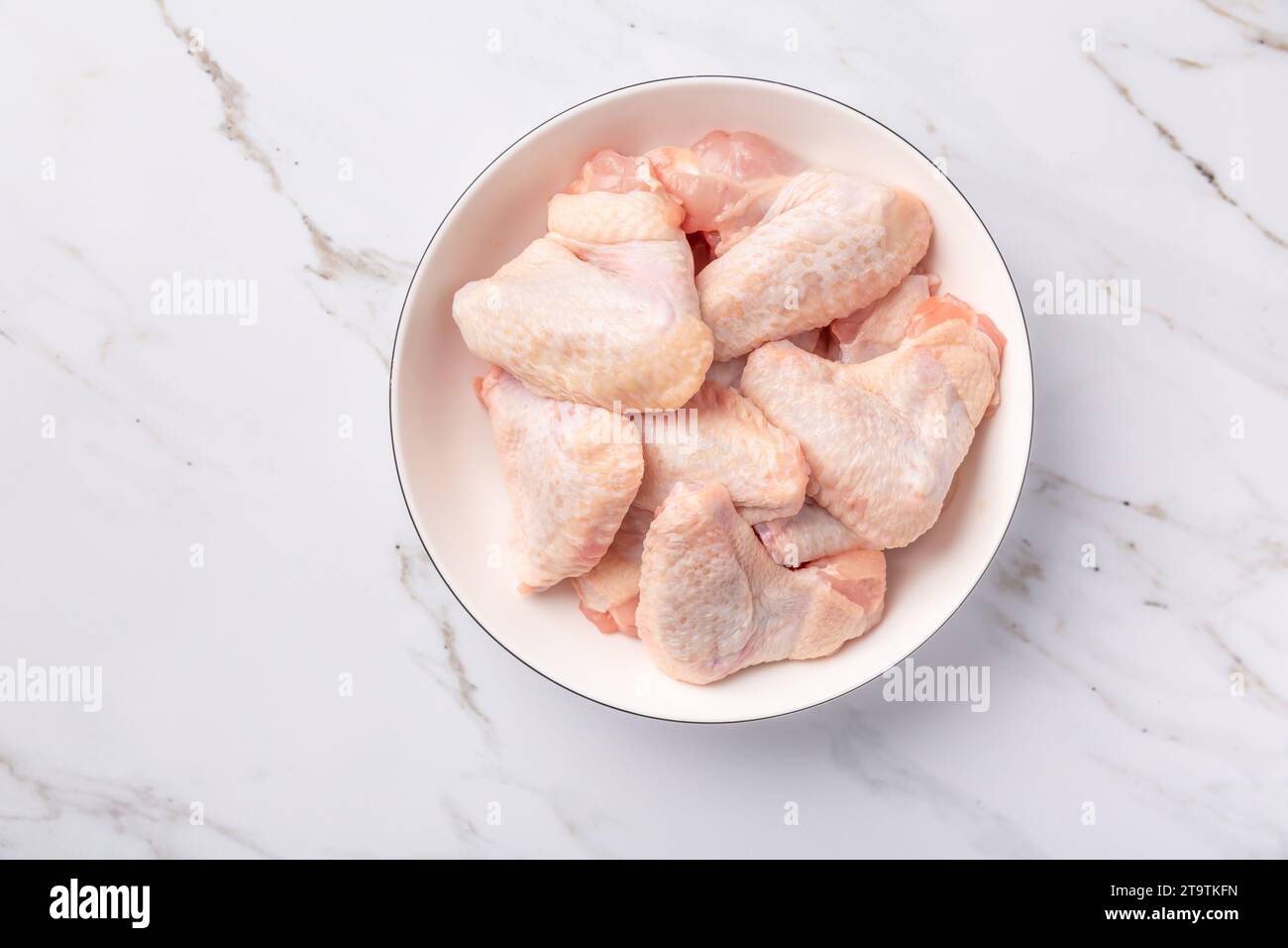 Raw chicken wings in white bowl, prepared for cooking on marble background Stock Photo