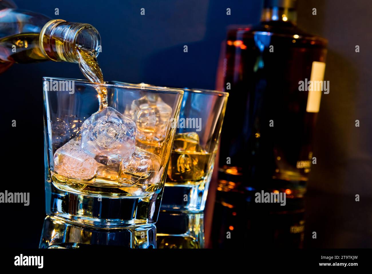 barman pouring whiskey in two glasses with ice cubes on table with light tint blue and reflection, time of relax with whisky Stock Photo