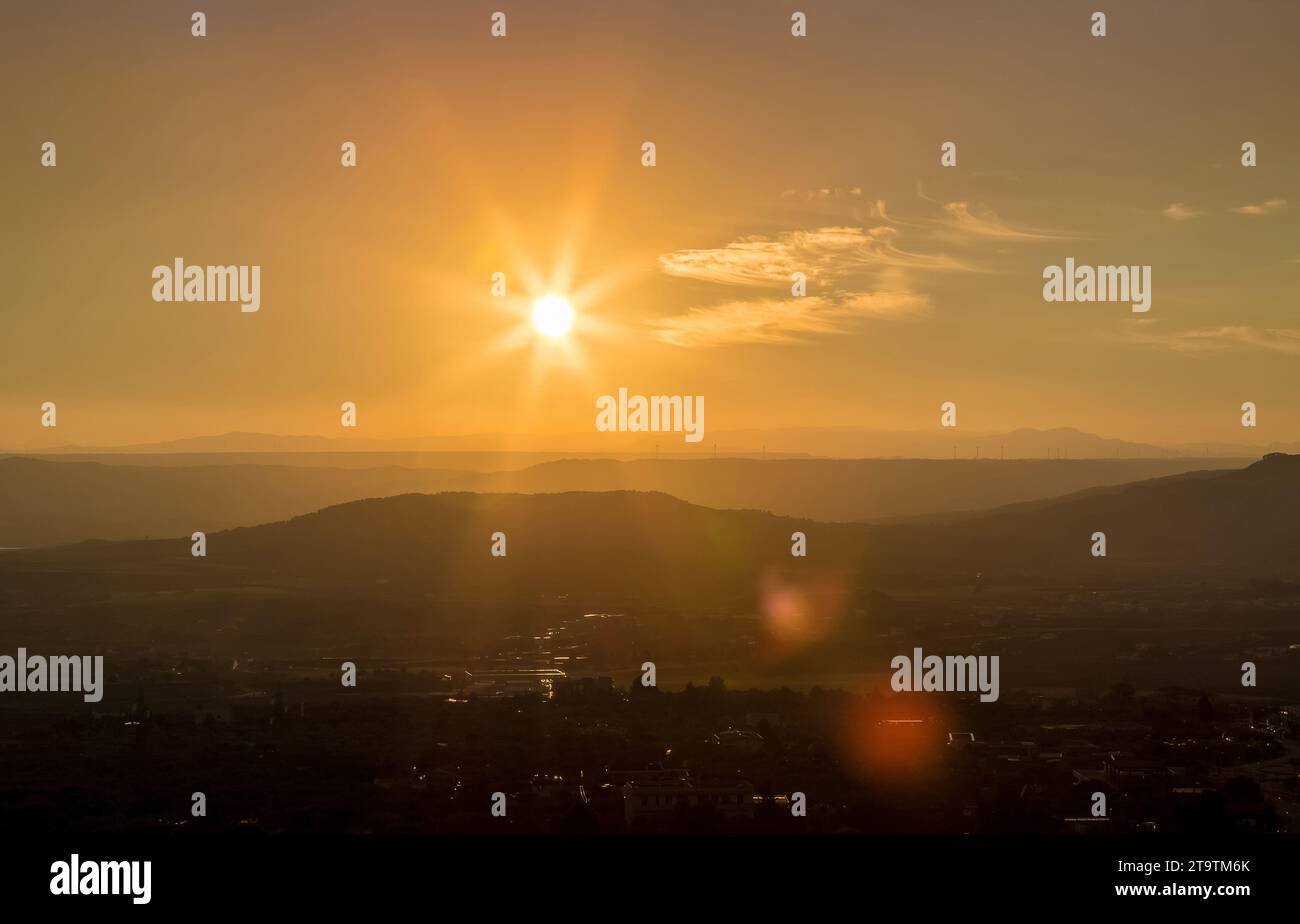 sunset scene with mountains in background, colorful sky with soft clouds and city in foreground, industrial view with sun light and lens flare Stock Photo