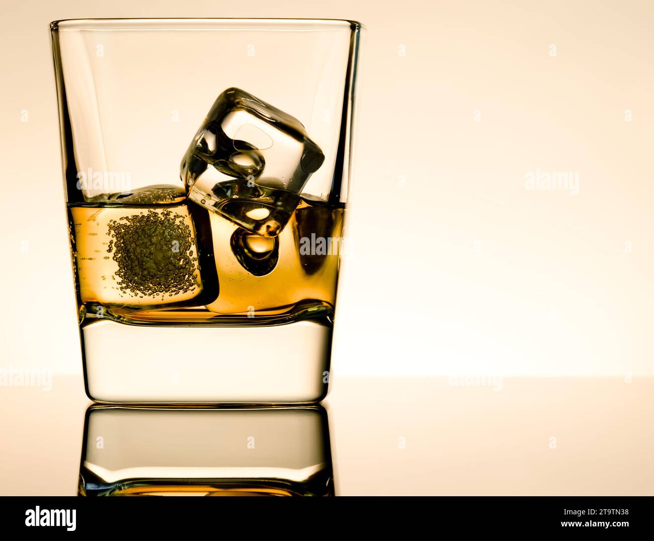 one glass of whiskey with ice cubes on table with reflection, light brown atmosphere, time of relax with whisky Stock Photo