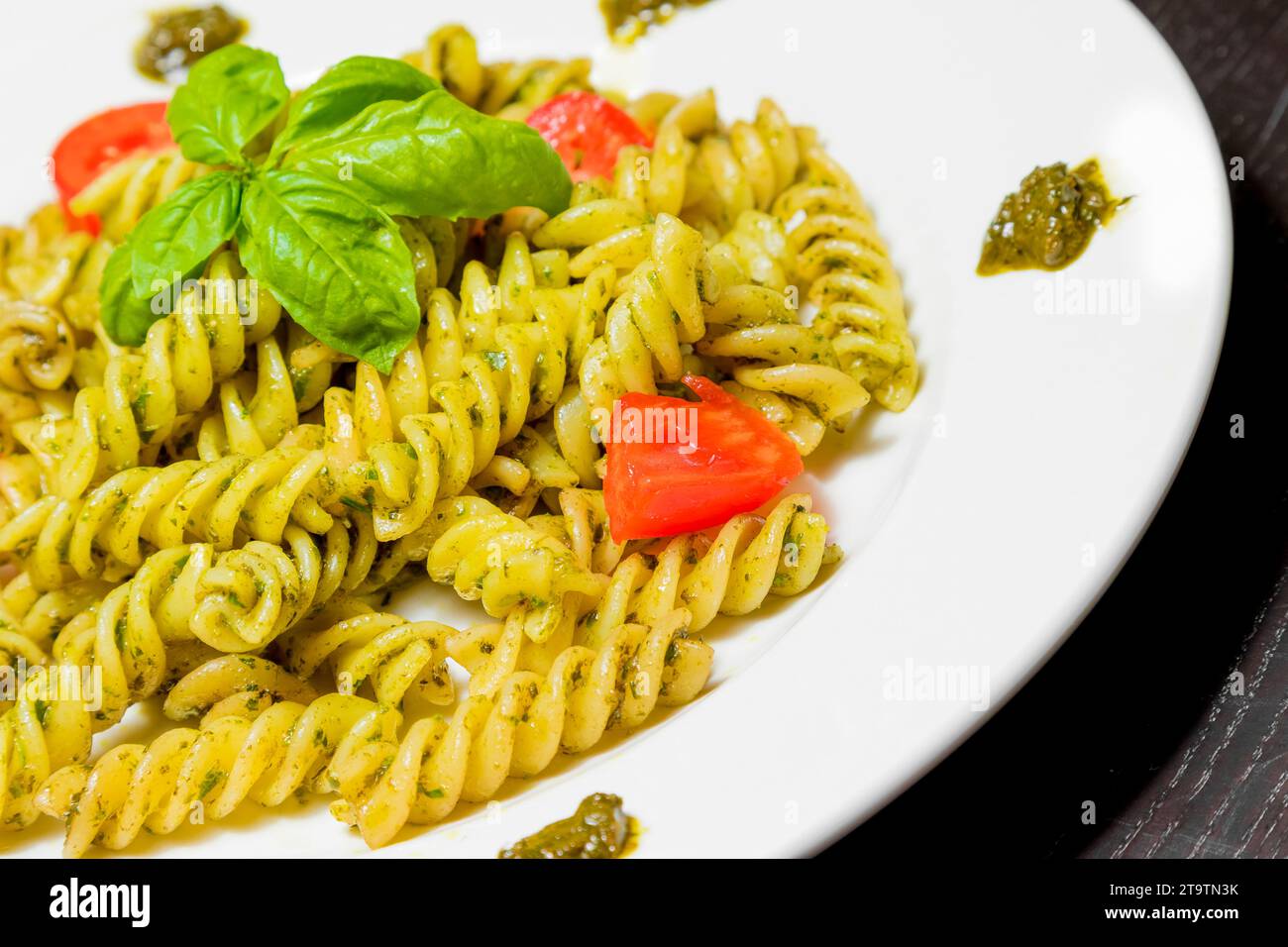 close-up of dish of pasta with pesto genovese sauce and vegetables, tomato and basil on black wood table Stock Photo