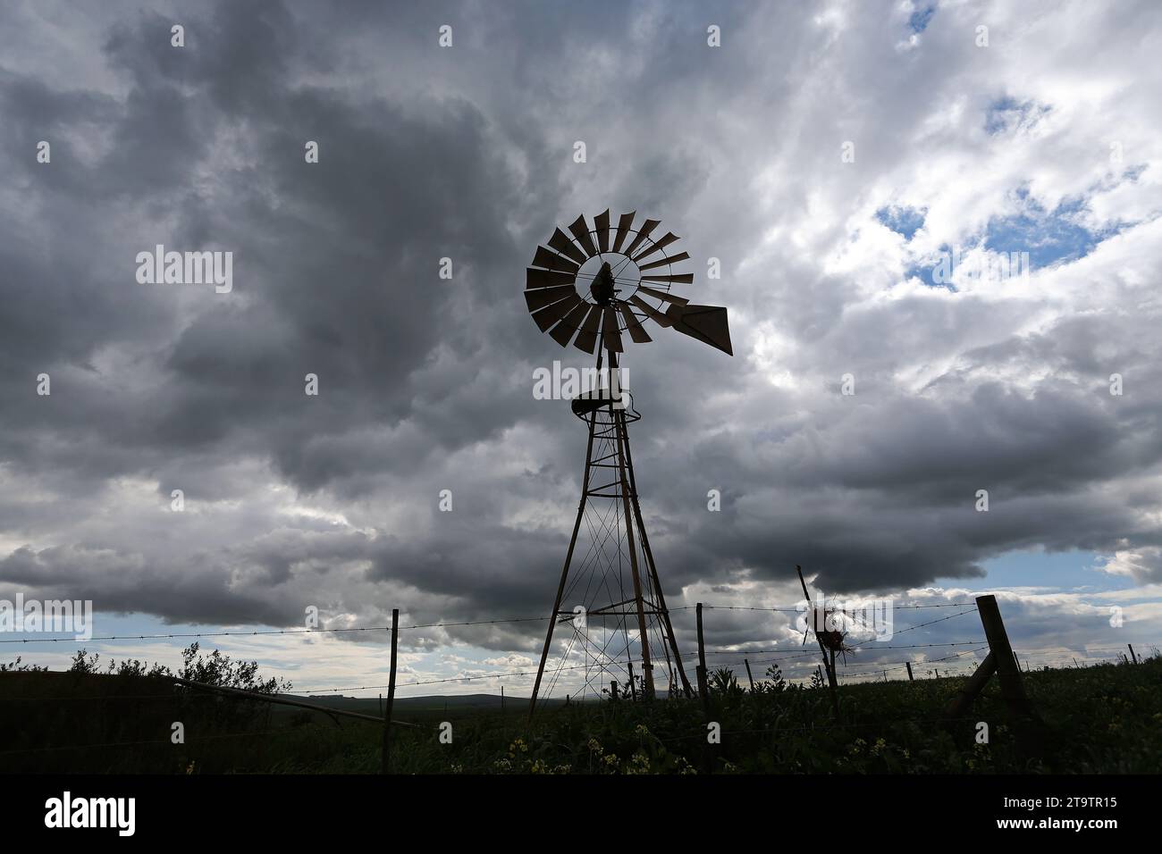 A silhouette of a water pump windmill against a cloudy sky on a farm in