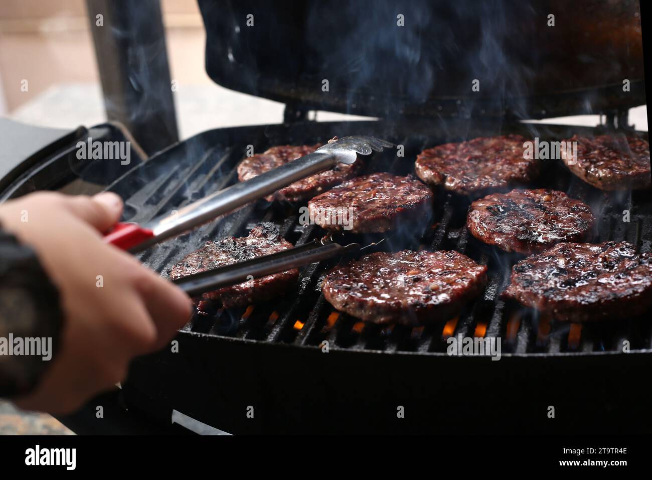 A General view of burger patties being turned on a gas grill Stock