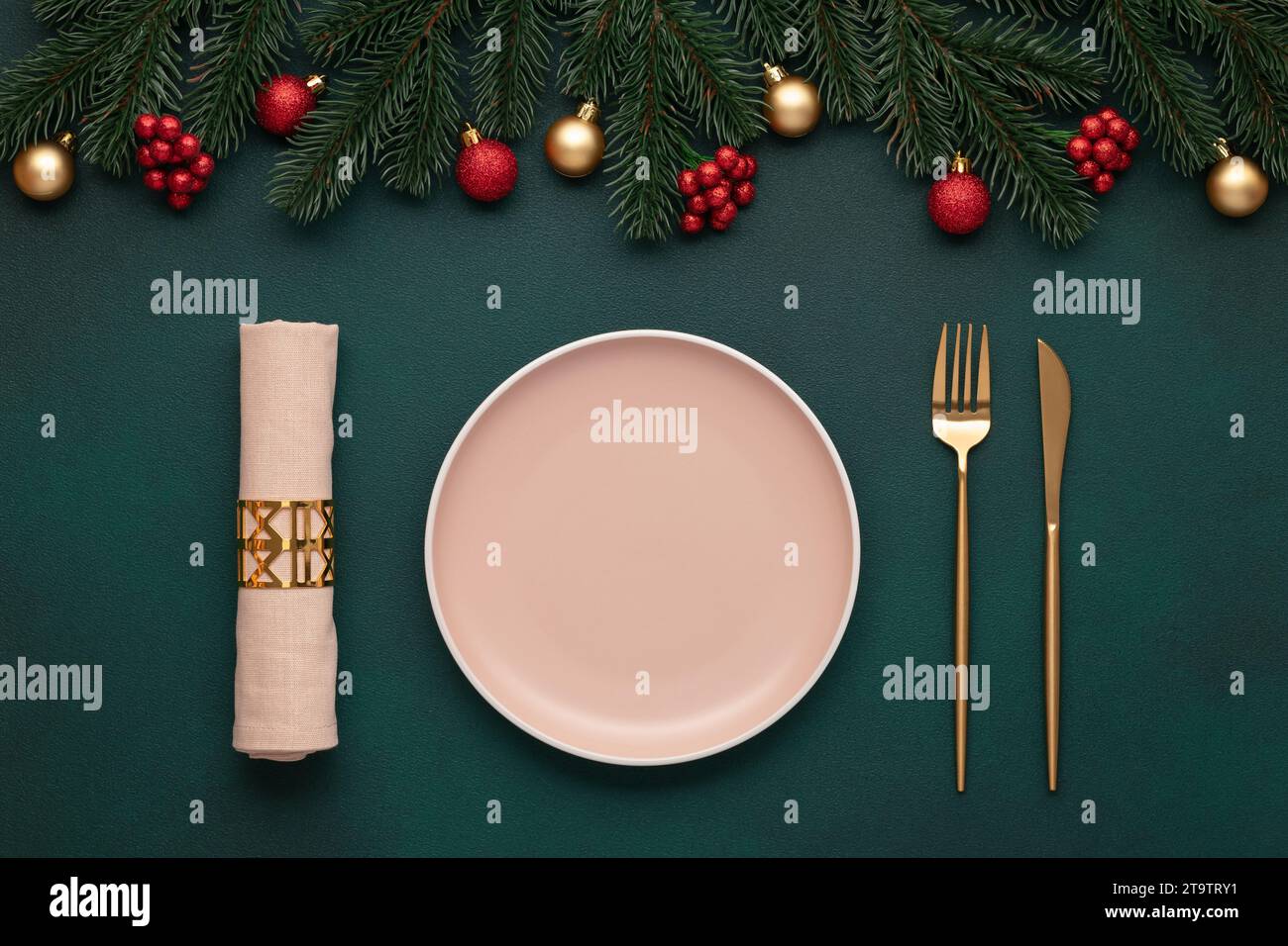 Christmas table with decorations. Empty plate, fork, knife. Gold cutlery, dark green background. Top view. Celebration place setting, evergreen tree. Stock Photo