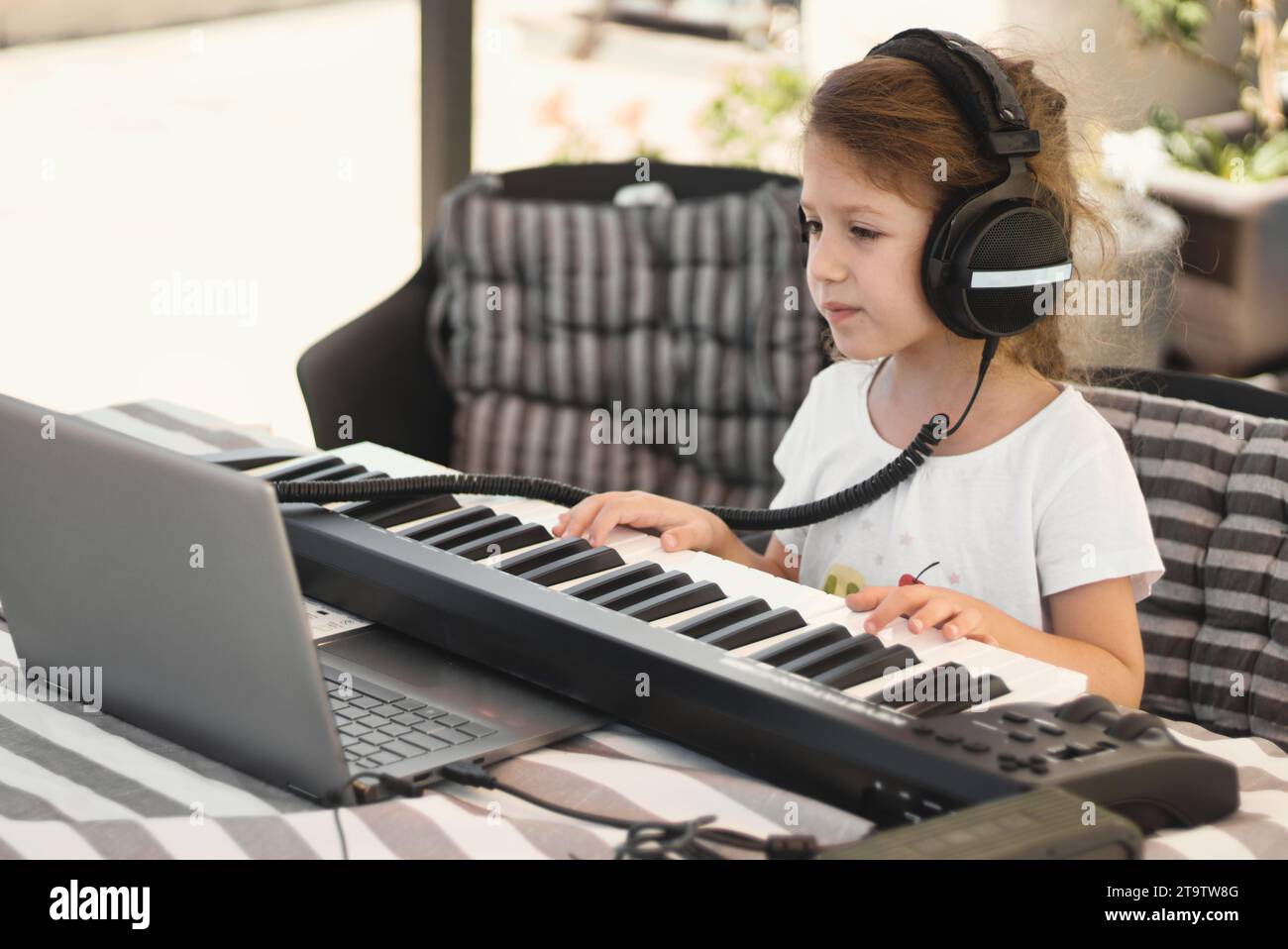 Behind Computer Keyboard A young white Caucasian girl wearing headphones and playing a MIDI ...