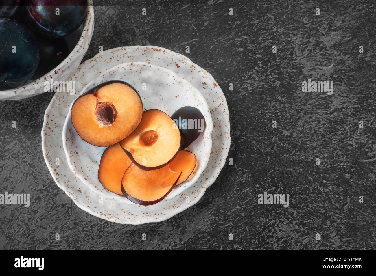Ripe plums on a handmade white kraft plate on a dark rustic background, fall. Top view, flat lay. Copy space. Stock Photo