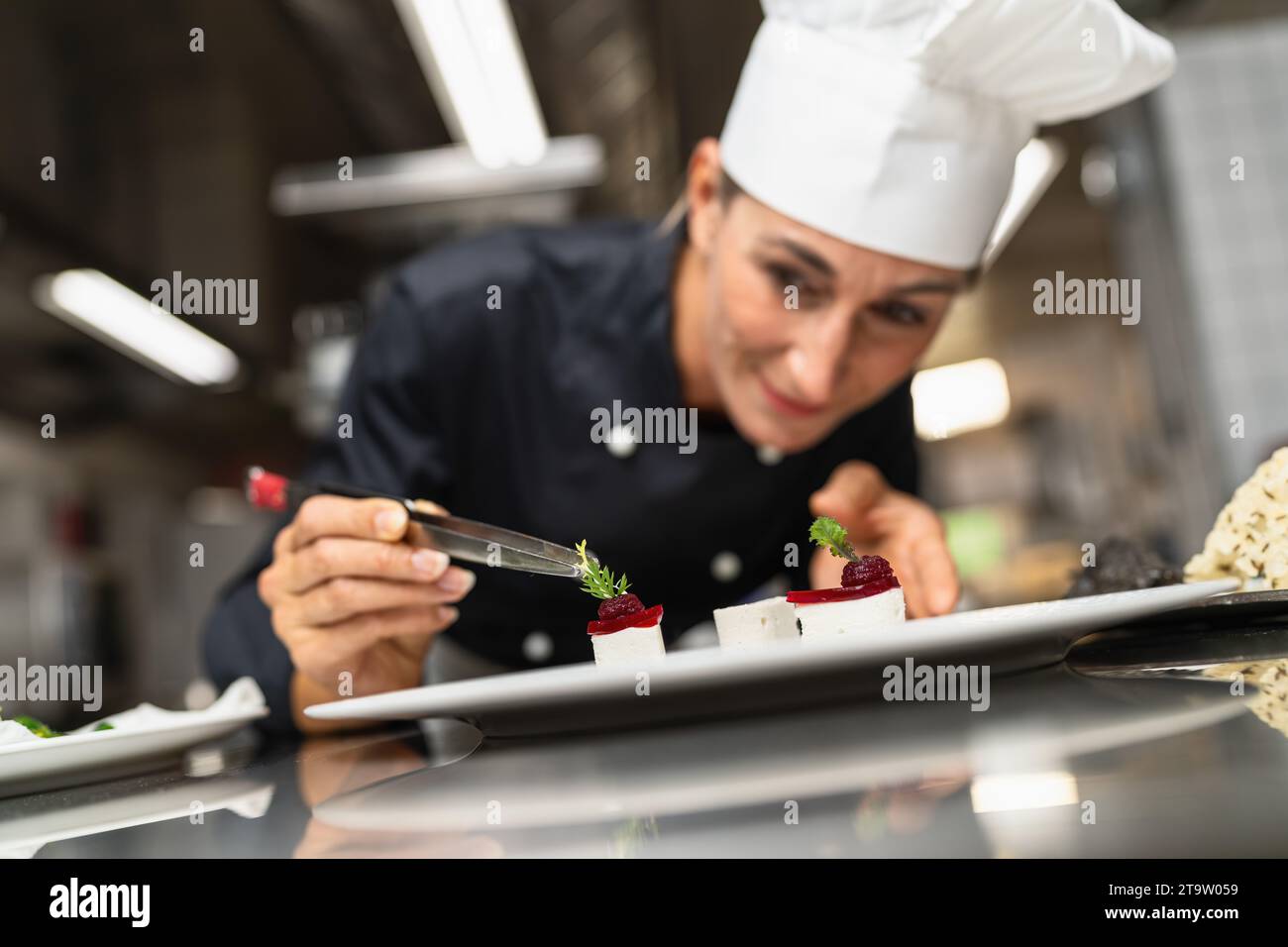 Chef Perfecting a Gourmet dessert adding green topping finishing dish, decorating meal in the end. Luxury hotel cooking concept image. Stock Photo