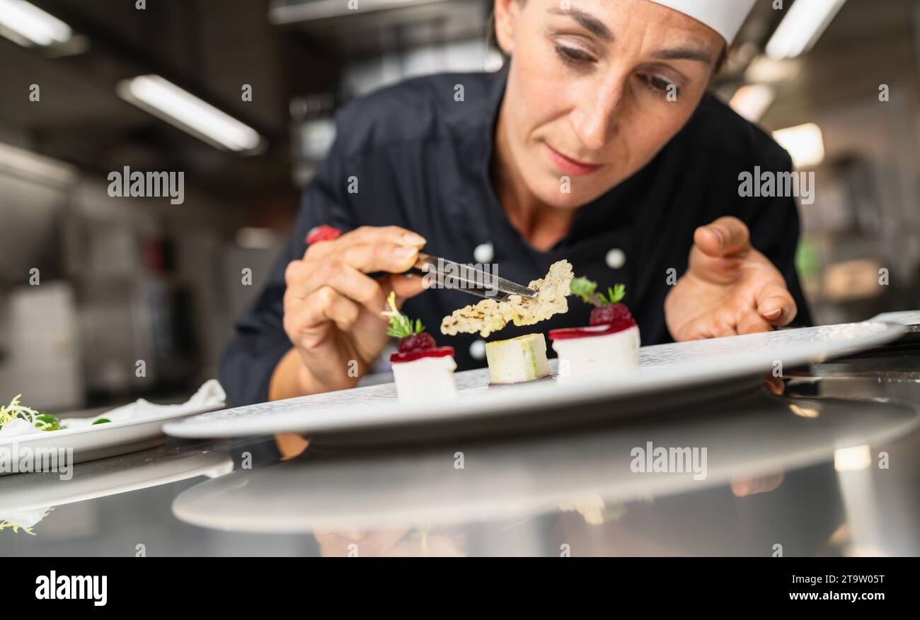 Chef Perfecting a Gourmet dessert adding rice chip topping finishing dish, decorating meal in the end. Luxury hotel cooking concept image. Stock Photo