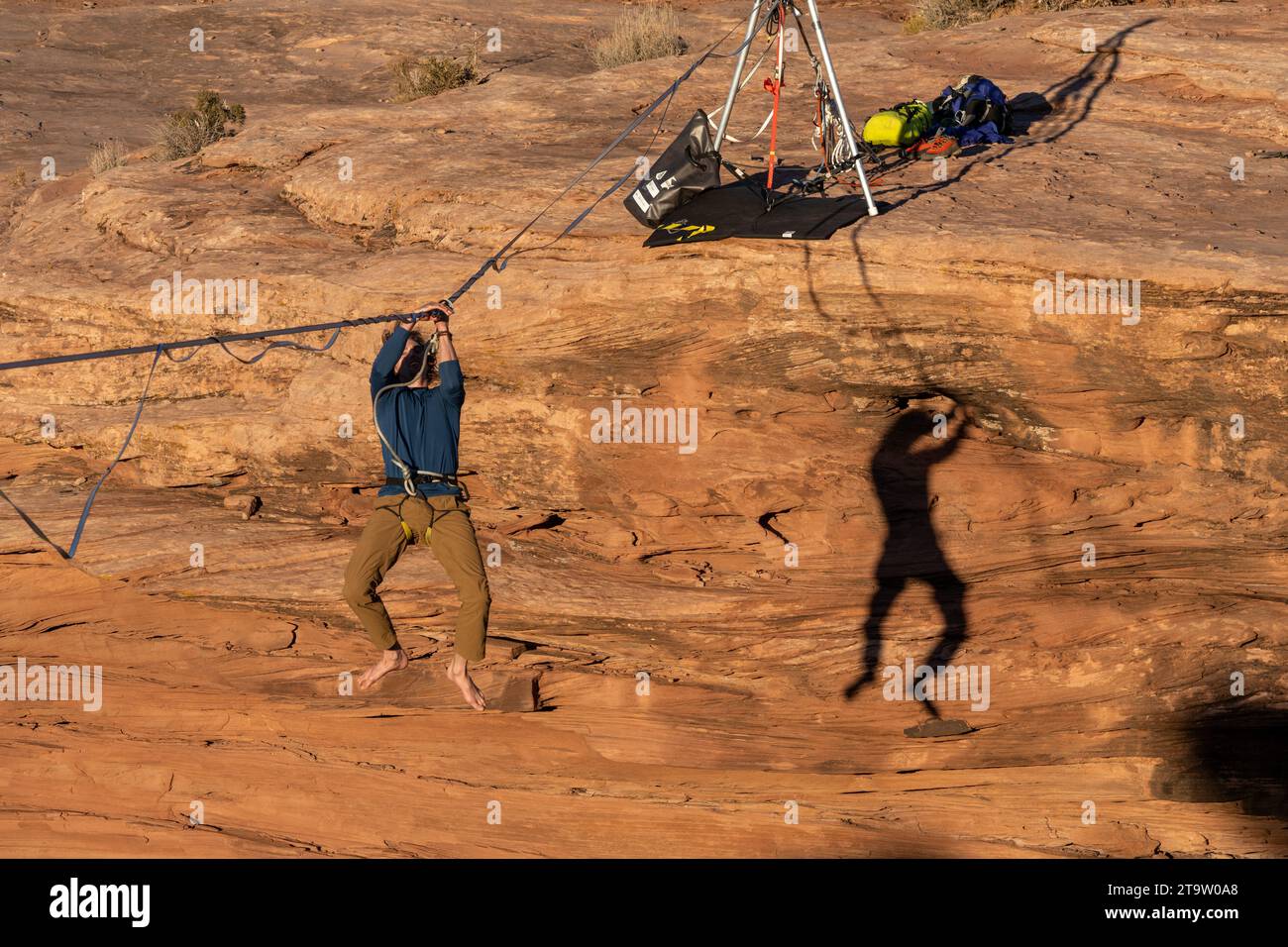A man with his shadow on the canyon wall hanging on the highline after a fall at the GGBY World Highline Festival near Moab, Utah. Stock Photo