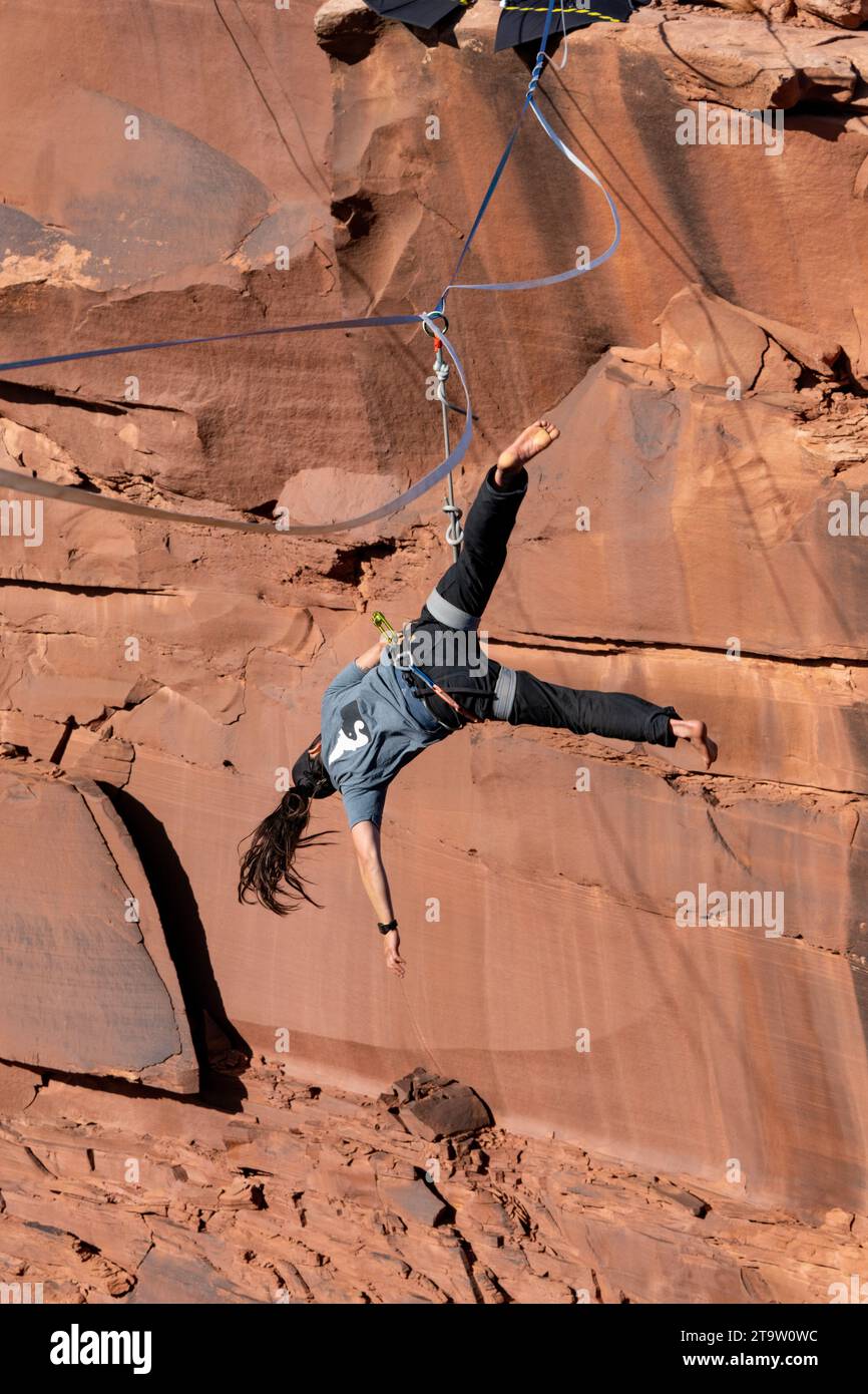 A female highliner loses her balance and falls off the highline, or whips, at a highline festival in Utah.  Her protective harness & leash keeps her f Stock Photo