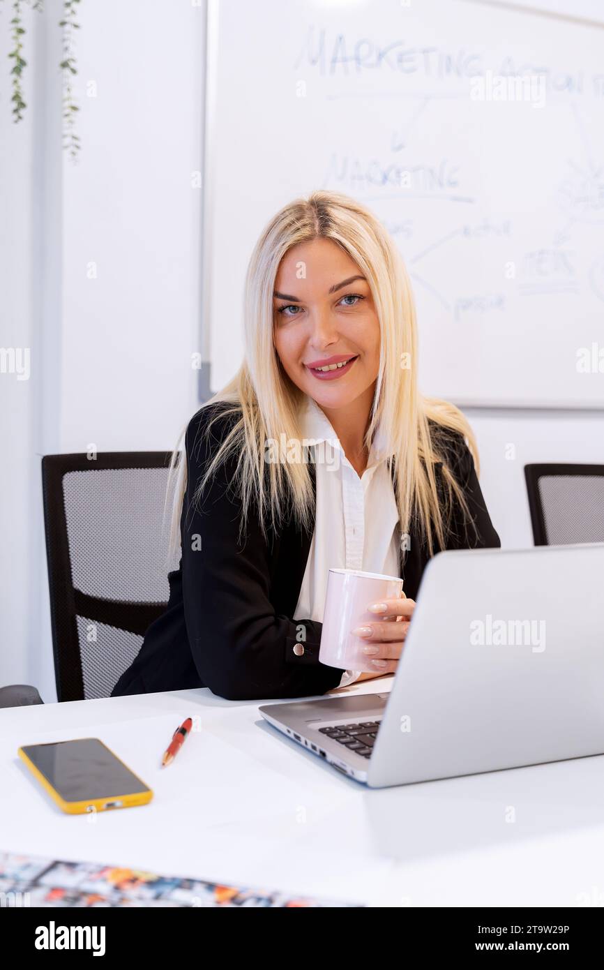 Businesswoman holding a cup of coffee while sitting at her desk in the ...