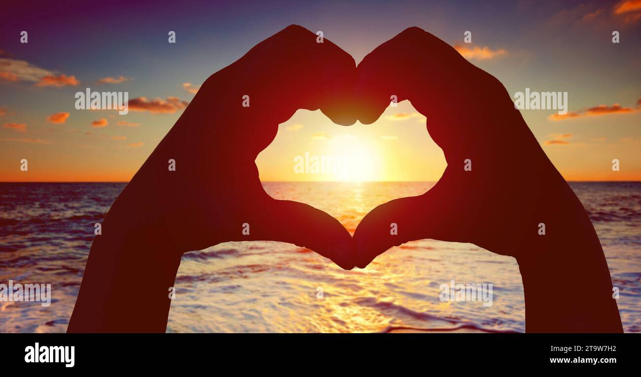 silhouette hands in heart shape with sunset in the middle and beach background, love concept Stock Photo