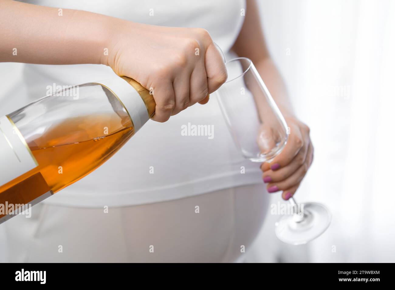 Pregnant woman pours an alcoholic drink into a glass. Negative effects of alcohol on the fetus Stock Photo