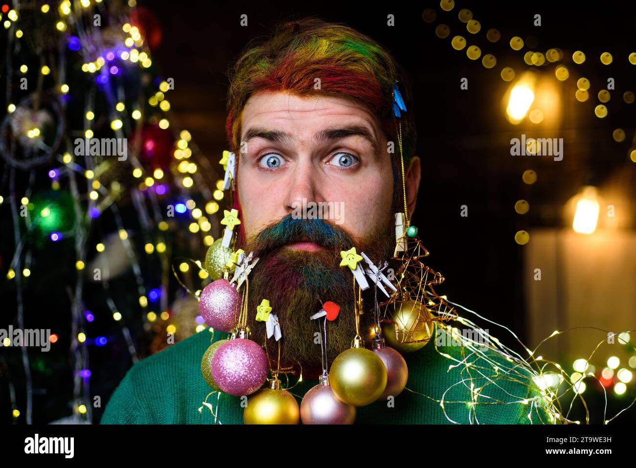 Christmas barbershop advertising. Bearded guy with decorated beard ready for Christmas or New Year party. Surprised man with colorful hair and beard Stock Photo