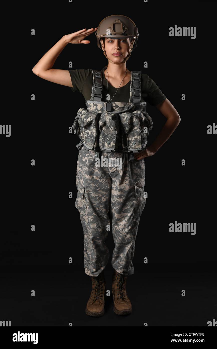 Confident young woman in military uniform saluting on black background ...