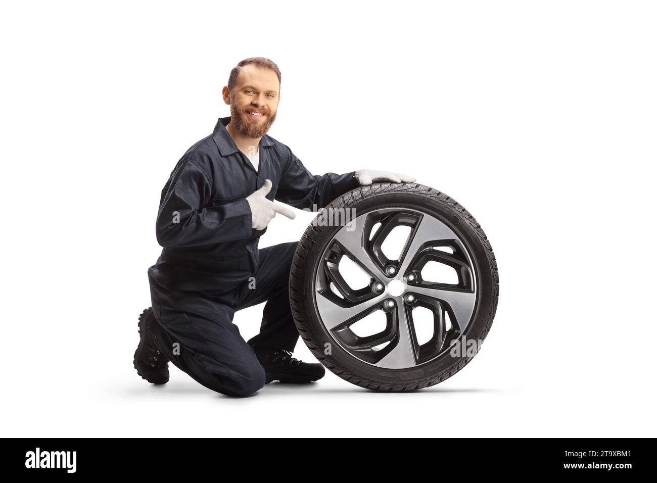 Car mechanic kneeling next to a tire and pointing isolated on white background Stock Photo
