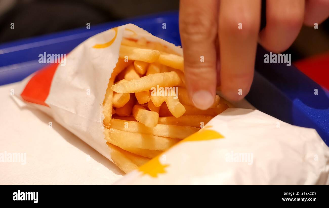 Man eating salted McDonalds fast food restaurant fries and a burger laying on a table, fingers, object closeup, nobody, shallow dof, quick meal set de Stock Photo