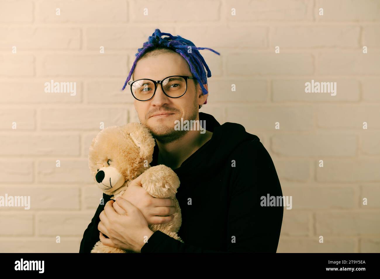 The Tender Embrace: A Man with Dreadlocks with Glasses Cherishing a Plush Toy. Stock Photo