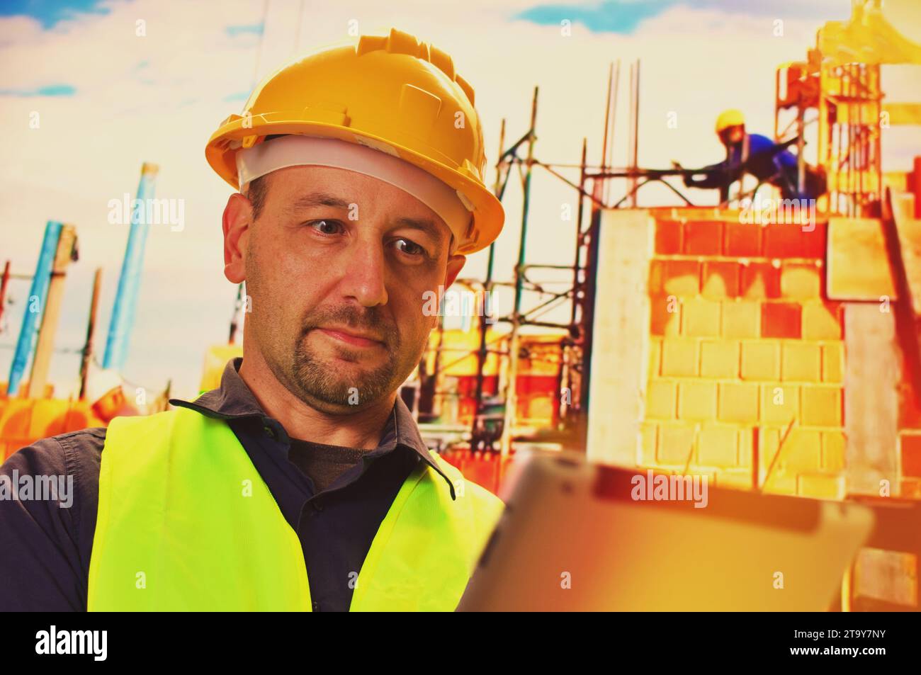 Construction worker with his uniform and hard hat is standing and using tablet Stock Photo