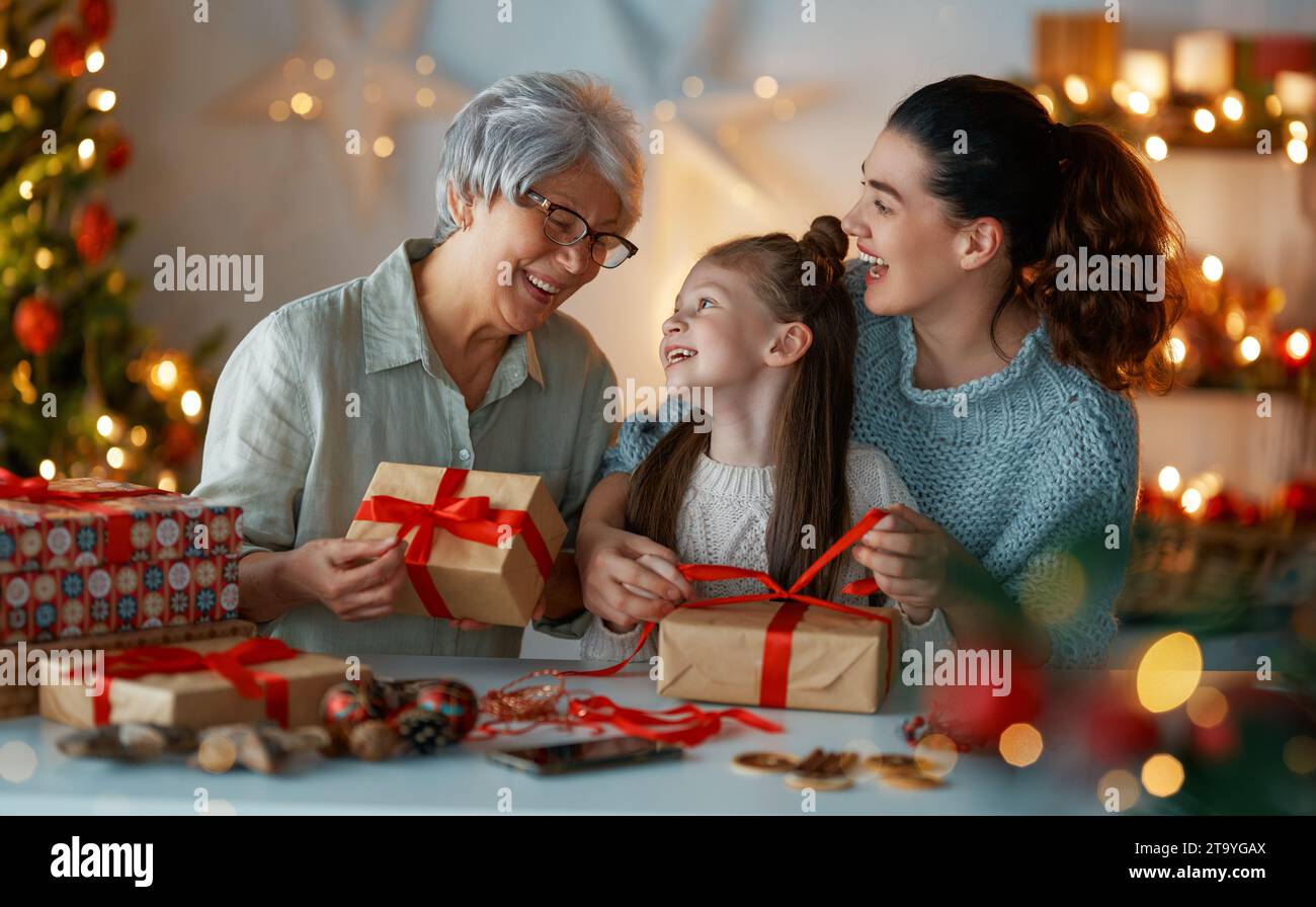 Happy Holidays. Cheerful grandmother, mother and cute daughter girl preparing for Christmas. People wrapping gifts, decorating home. Loving family wit Stock Photo