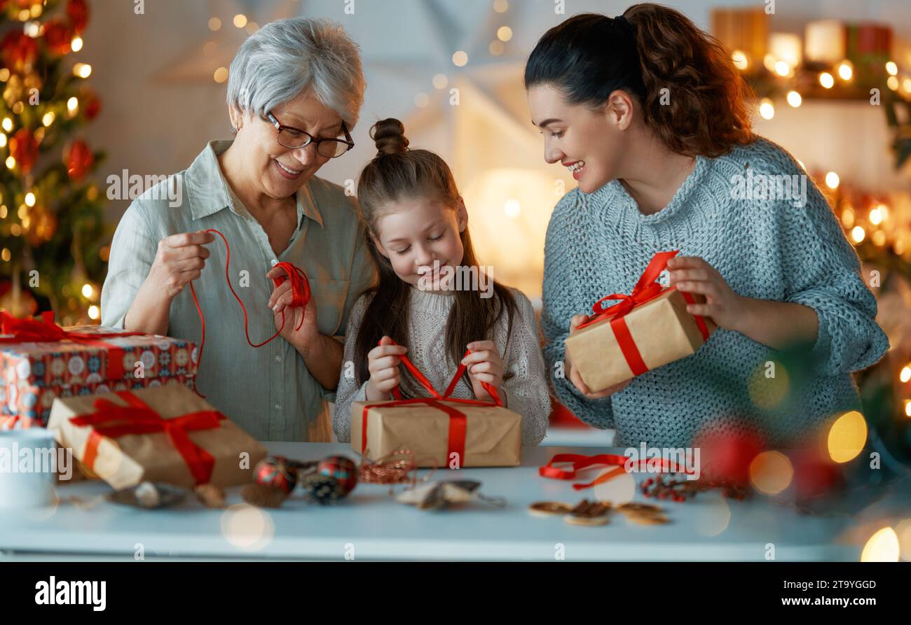 Happy Holidays. Cheerful grandmother, mother and cute daughter girl preparing for Christmas. People wrapping gifts, decorating home. Loving family wit Stock Photo