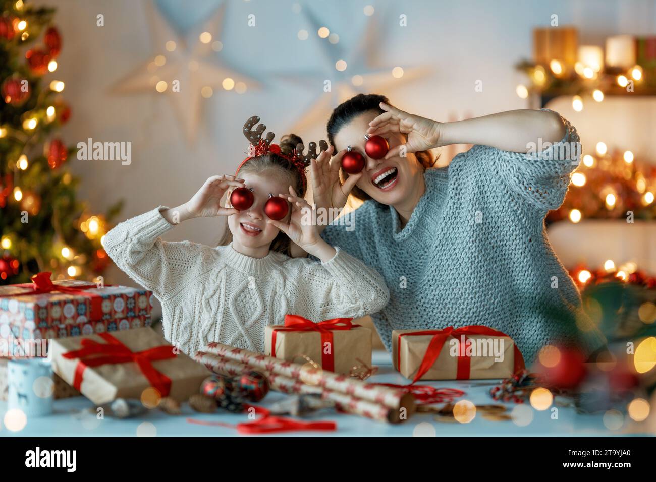 Happy Holidays. Cheerful mother and her cute daughter girl preparing for Christmas. People wrapping gifts, decorating home. Loving family with present Stock Photo