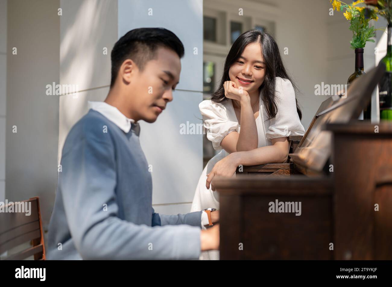 A beautiful young Asian girl is admiring at her boyfriend while he is playing piano in a garden. couple concept Stock Photo