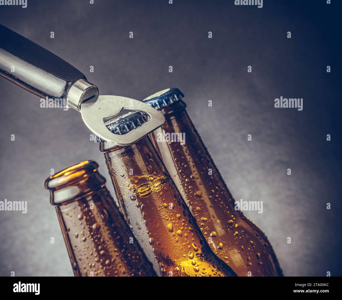 three fresh cold beer ale bottles with drops and stopper open with bottle opener on dark background Stock Photo