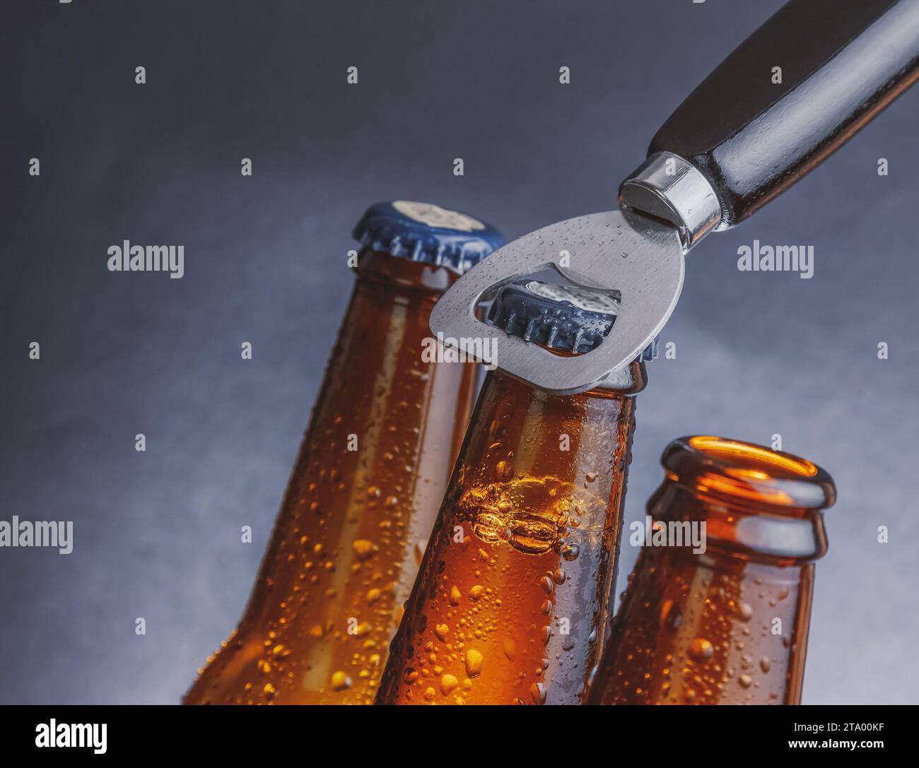 three fresh cold beer ale bottles with drops and stopper open with bottle opener on dark background Stock Photo