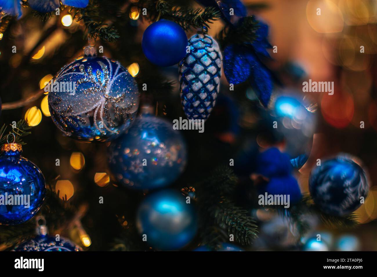 Bright blue Christmas ball with silver ornament hanging on the Christmas tree with golden garland lights. Decorated spruce branches. Stock Photo