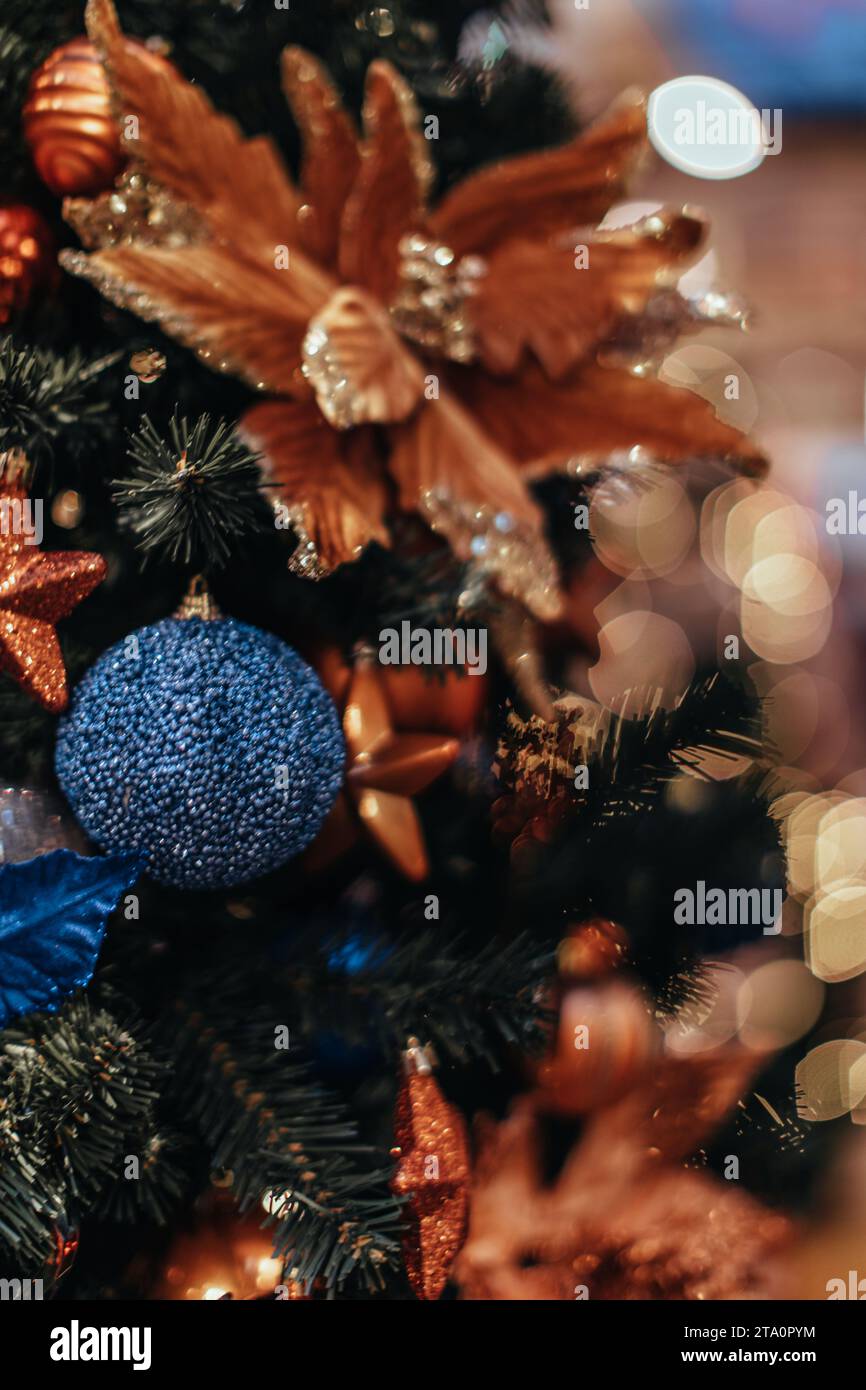 Golden flower and blue Christmas ball hanging on a Christmas tree with garland lights. Decorated spruce branches. Stock Photo