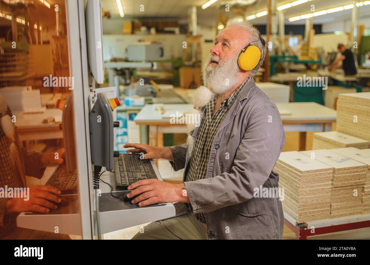 Man using computer on a cutting machine in a woodworking workshop Stock Photo