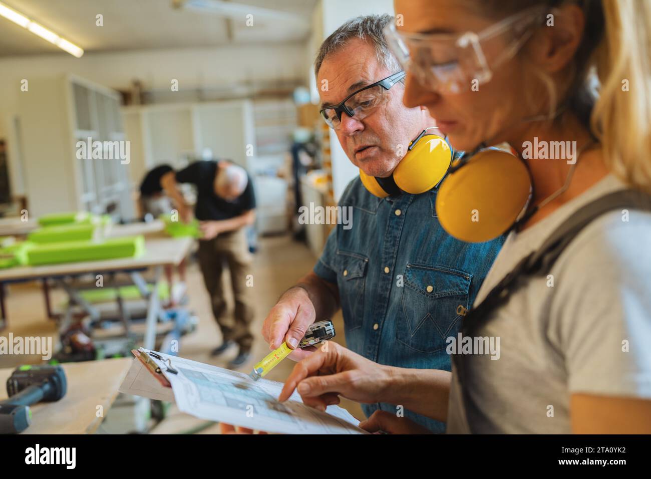 Two carpenters reviewing a blueprint with another working in the background Stock Photo
