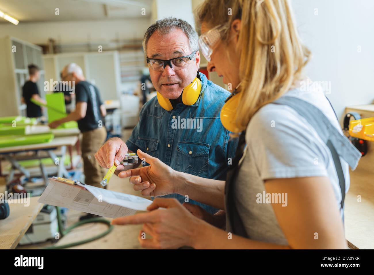 Instructor explaining measurements on blueprint to apprentice in a carpentry workshop Stock Photo